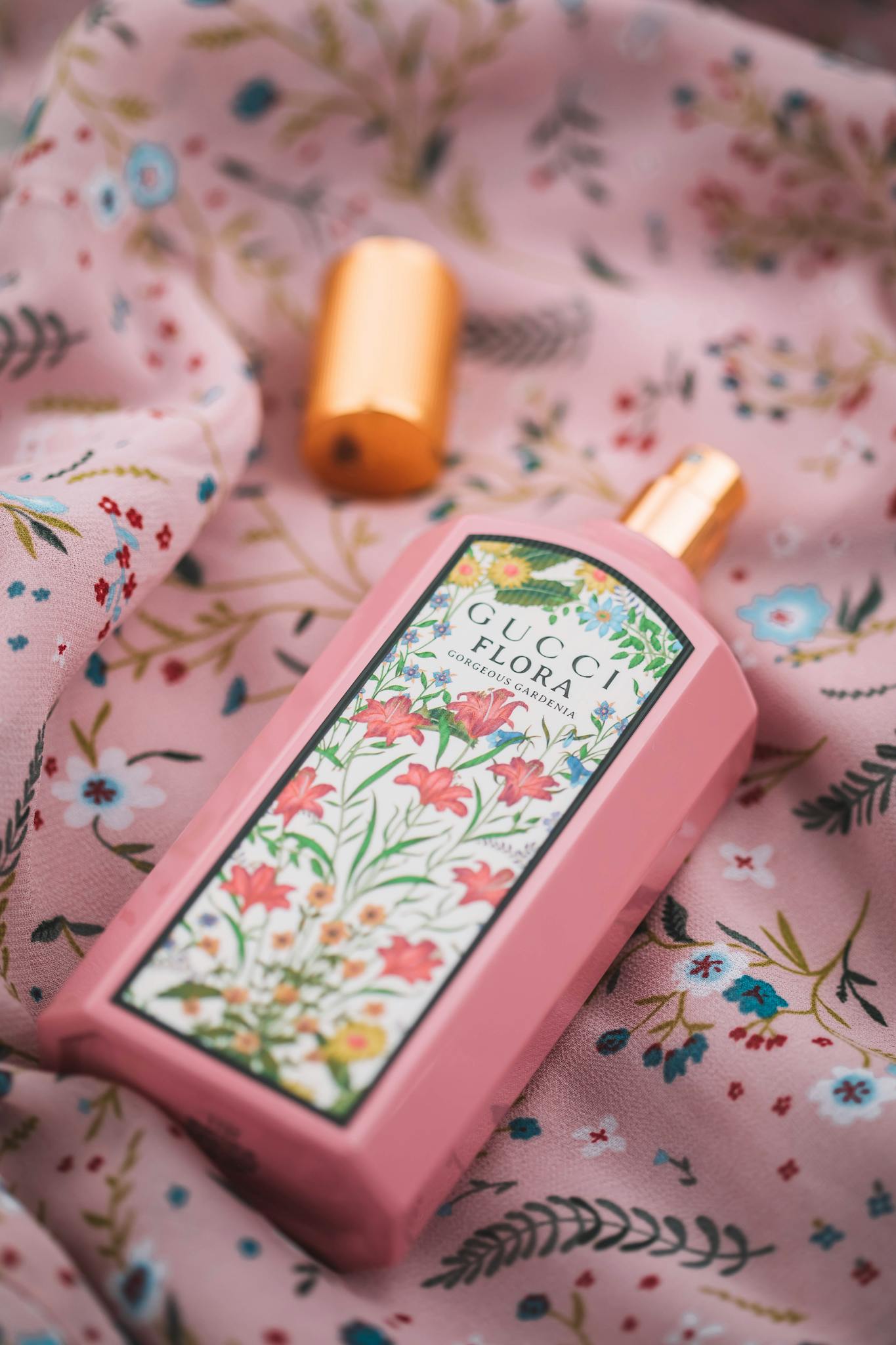 Close-up of an open pink Gucci Flora perfume bottle on floral fabric, indoors.