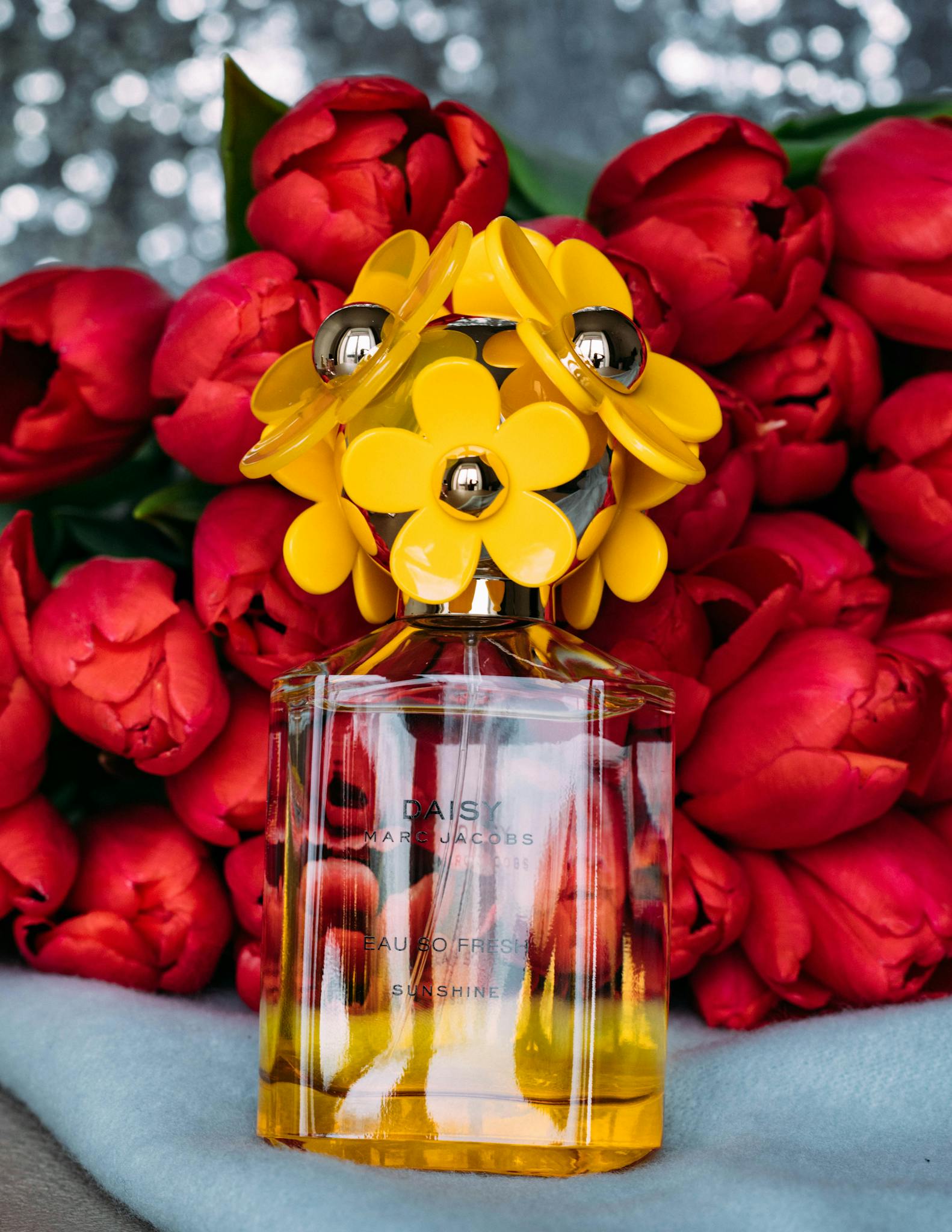 Colorful perfume bottle with bright red tulips, captured indoors for elegant floral decor.